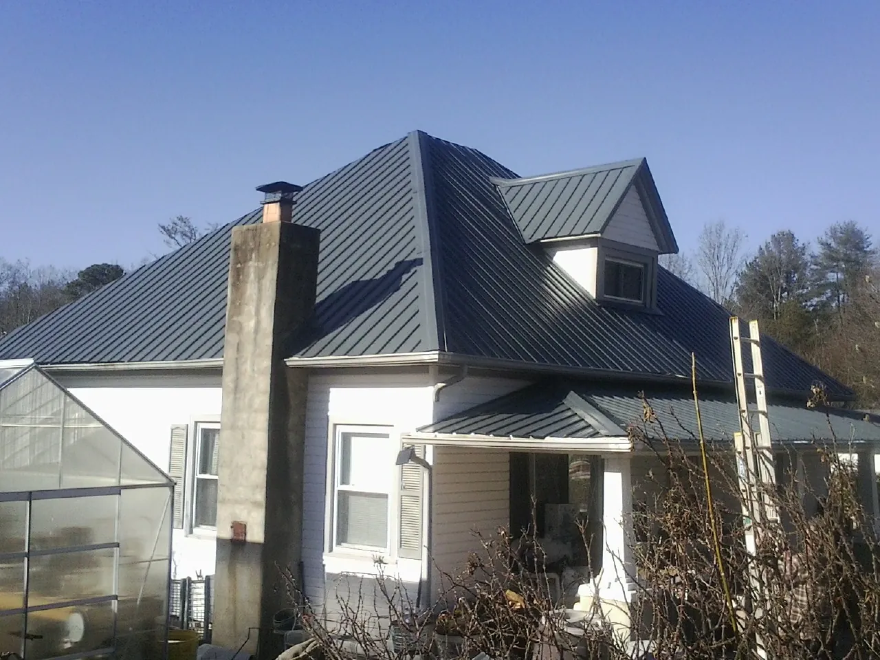 Dark blue standing seam metal roof on a white farmhouse with dormer — Slate & Tile Roof Repair by Roofing Brothers in Baxter