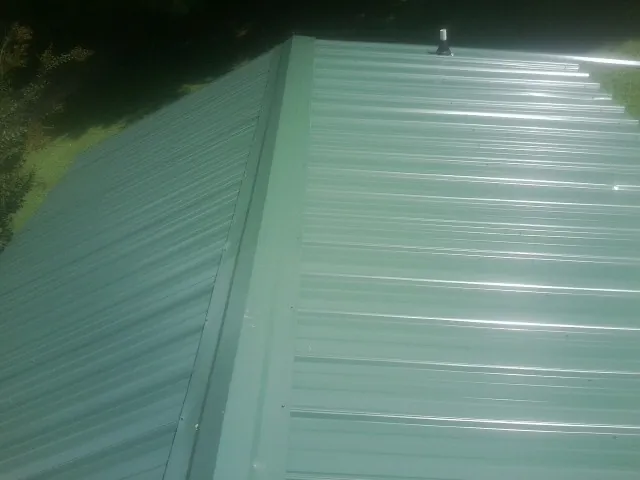 New green metal panels meeting at the ridge of a roof — Flat Roof Repair work by our crew in Baxter