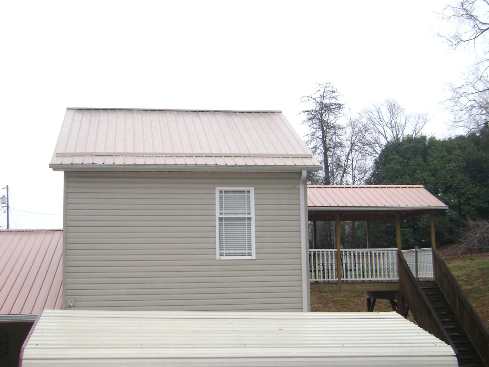 Tan metal roofs on a two story addition and attached porch, from a Roof Replacement job in Baxter